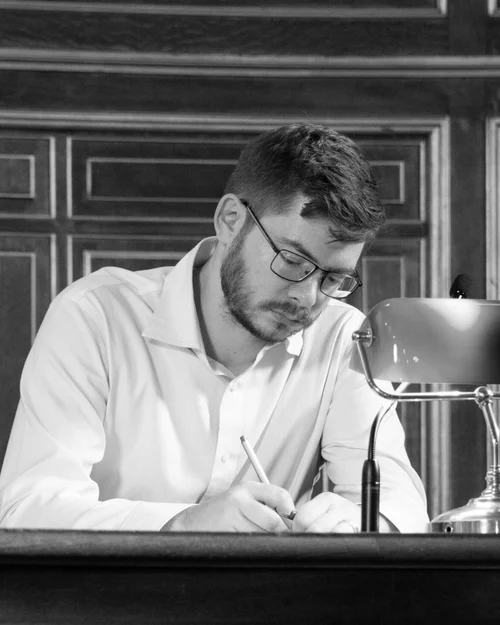 Yannick Rochat writing at a desk in a wood-panelled hall, beside a banker's lamp
